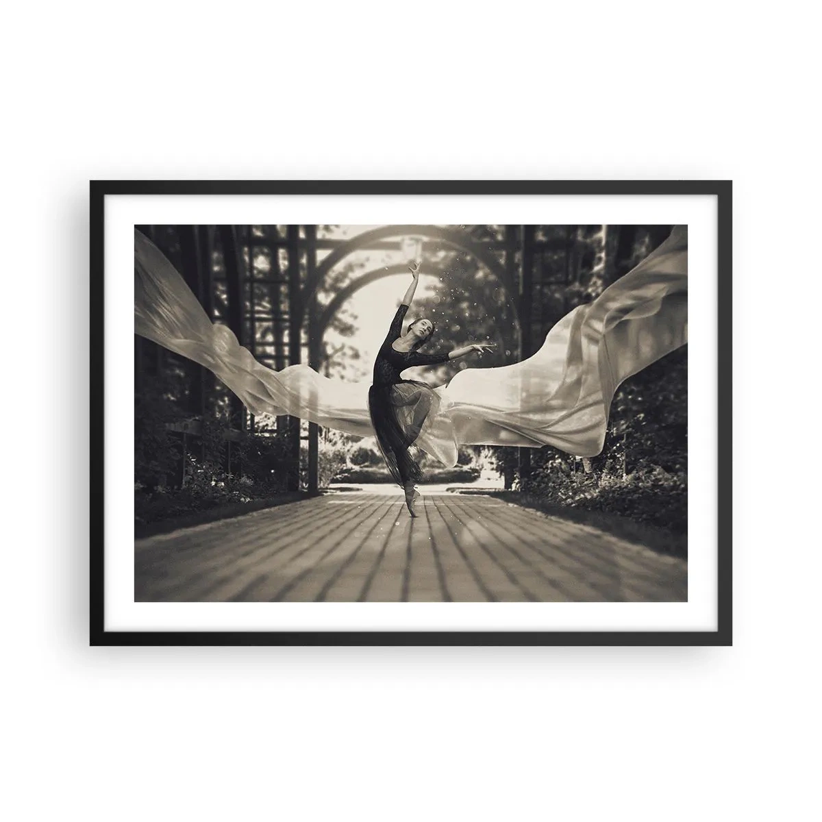 Affiche dans un cadre noir - Poster - Une danseuse vêtue d'une robe fluide exécute un saut sur fond de jardin noir et blanc. - 70x50cm - La danse de l'esprit jardin - Décoration murale moderne pour le salon et la chambre ARTTOR