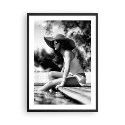 Affiche dans un cadre noir - Poster - Une photographie en noir et blanc d'une femme portant un chapeau assise au bord de l'eau. - 50x70cm - Rêve d'été - Décoration murale moderne pour le salon et la chambre ARTTOR